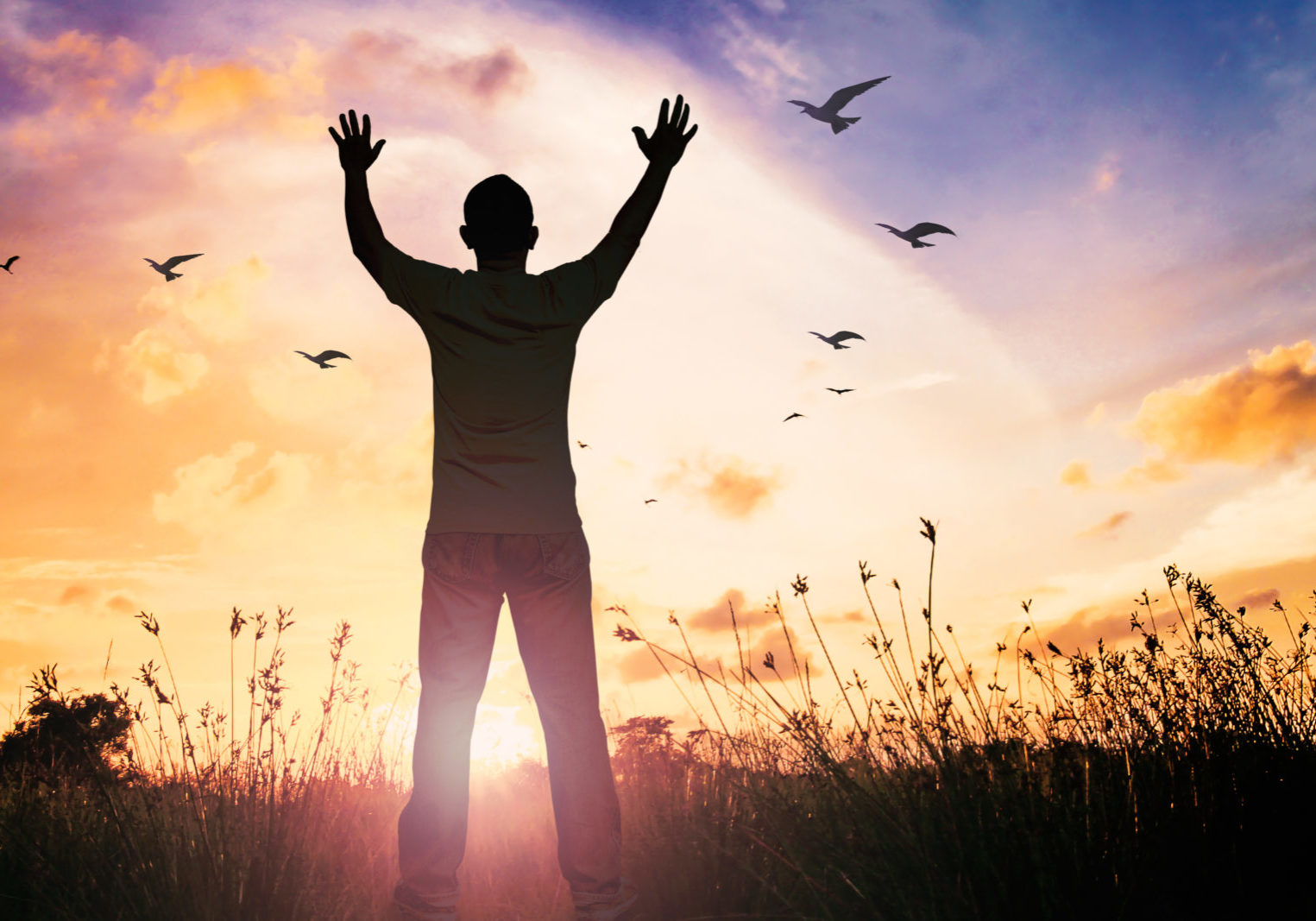 man holding hands up to the sky in front of a sunrise